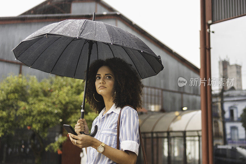 一名年轻女子在雨天用智能手机等出租车