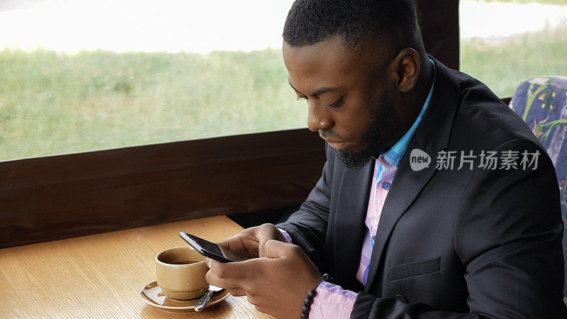 非裔美国商人坐在咖啡馆里用智能手机输入信息。