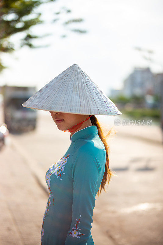 身穿越南传统旗袍的妇女，头戴锥形帽子