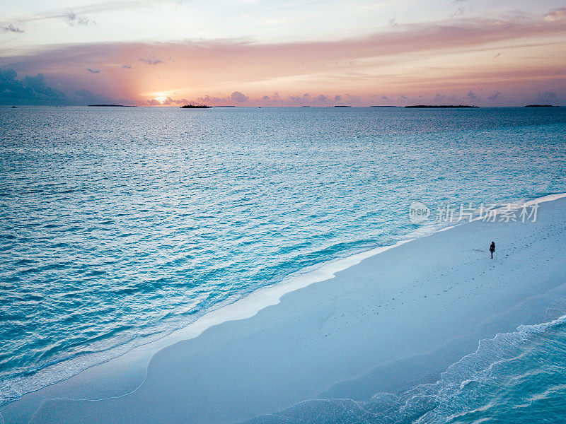日落时分，年轻的成年女子站在马尔代夫碧绿的沙滩上