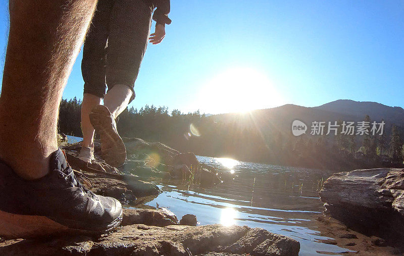 日出时分，一对夫妇沿着湖边的岩石散步