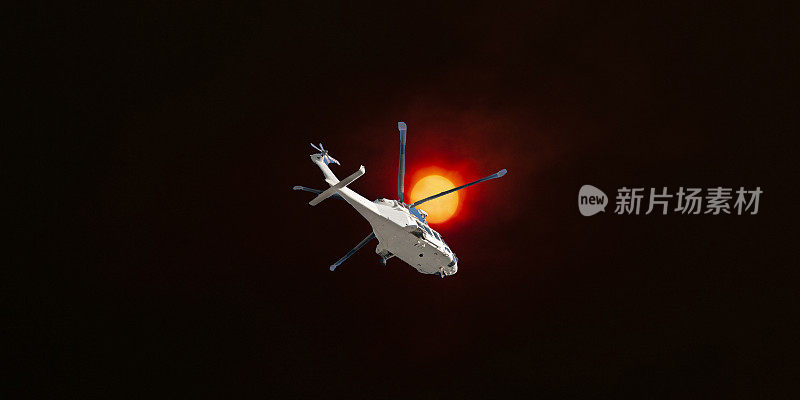 戏剧性的森林大火日落天空与一架空中直升机在前景。太阳透过野火的烟雾和薄雾照耀着高斯福德市。2019年澳大利亚。