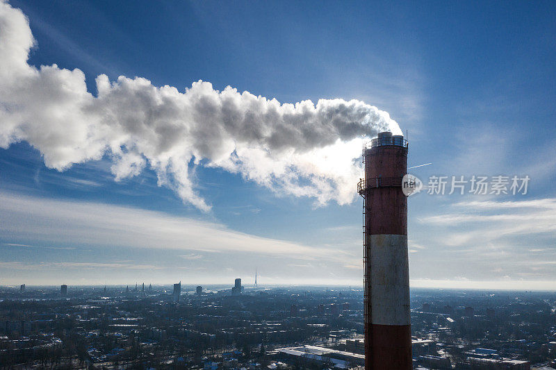 暖气站的烟囱和烟雾弥漫在冬天蓝色的天空中