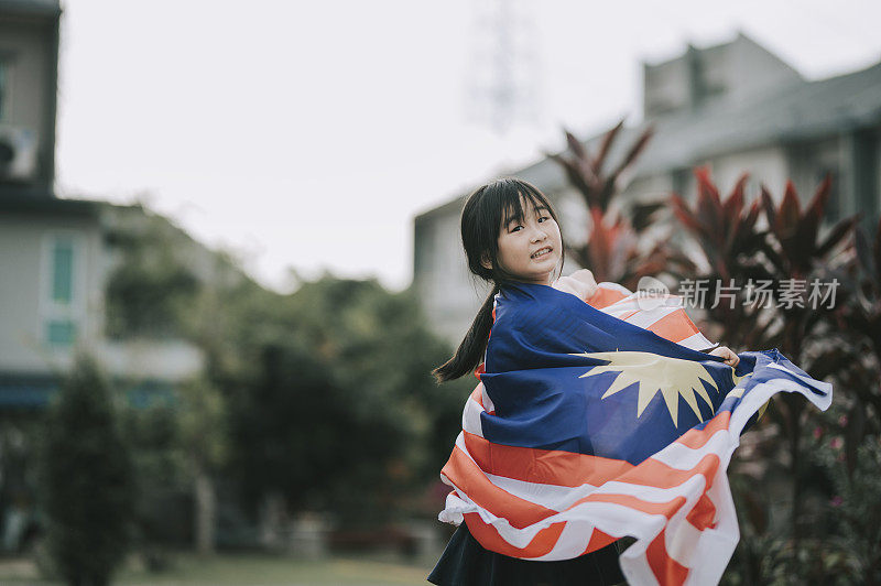 一个裹着马来西亚国旗的亚洲华裔小女孩在公园转身