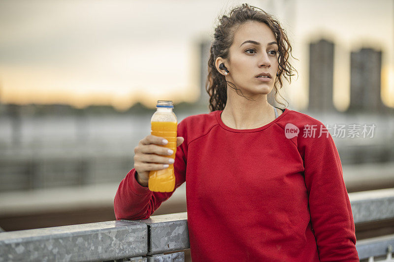 口渴的运动女性在桥上慢跑后休息和喝橙汁