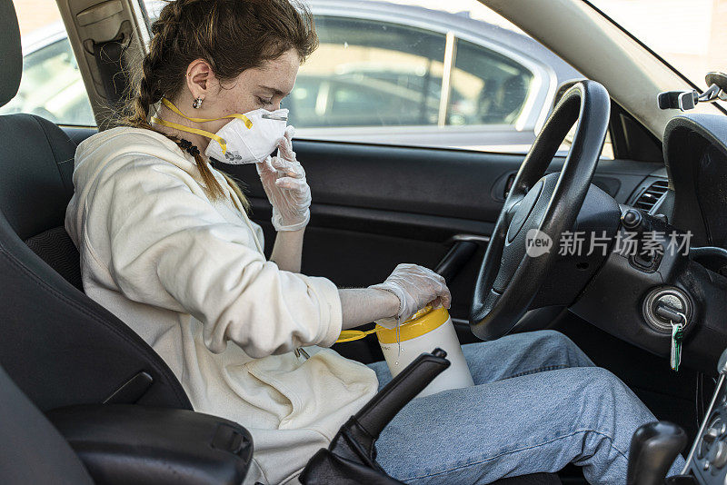 一名年轻女子戴上防护口罩，坐在车内用消毒湿纸巾清洁双手，从容器中取出消毒湿纸巾