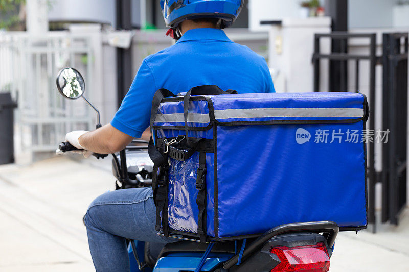 快递员穿着蓝色制服，骑着摩托车和快递箱。摩托车送食品或包裹快递服务