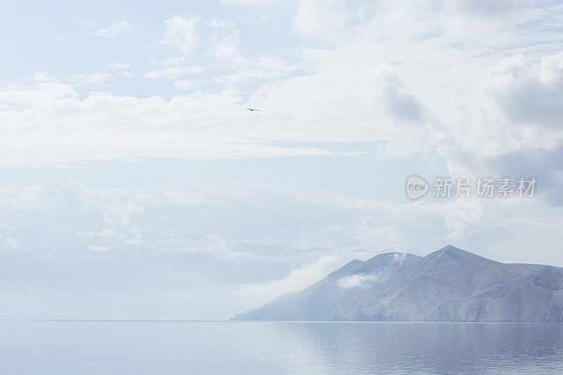 越过平静的大海看到远处山丘上的云