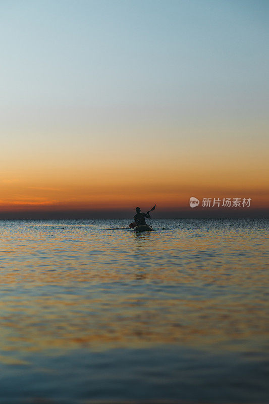 在桑给巴尔岛美丽的日落中，一个年轻人在海洋中划着皮艇