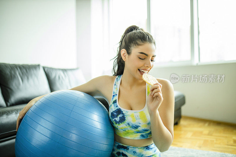 年轻女子在高强度的家庭锻炼后，穿着运动服吃米饼