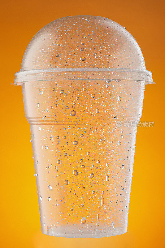 空塑料外卖杯，水杯。冰冷的一次性杯子，与水滴凝结在橙色的背景