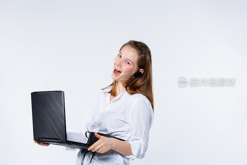 白种人金发女人微笑着，拿着笔记本电脑，看着镜头，在浅灰色的背景上为成功而兴奋。年轻自信的女商人在网上工作，流媒体博主