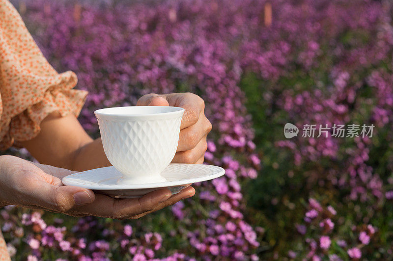 女性手捧咖啡或茶杯，手捧花坛位置。