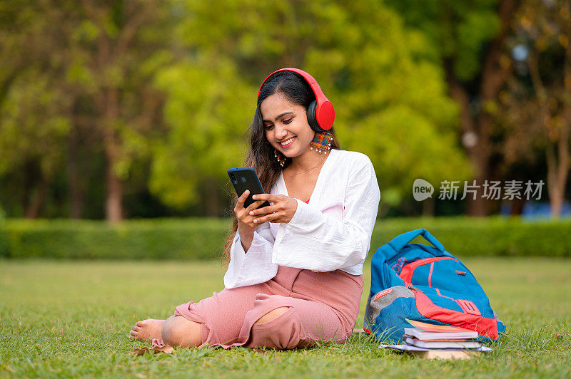 年轻女学生在校园公园用手机和耳机看视频