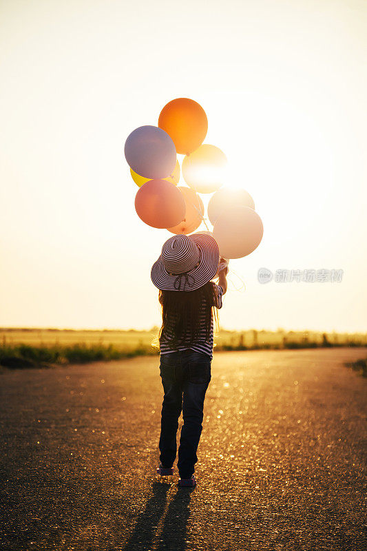 小女孩拿着彩色气球飞向夕阳。心理健康、正念、当下、自由、希望的概念