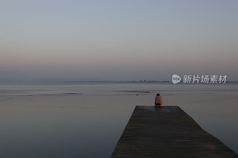 一个女人坐在木码头上望着大海