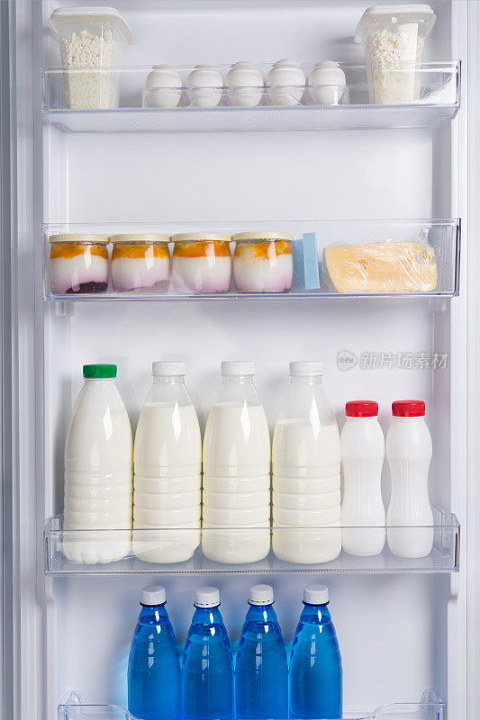 在白色冰箱的门上，架子上放着鸡蛋、奶酪、酸奶、白软干酪、牛奶和瓶装水
