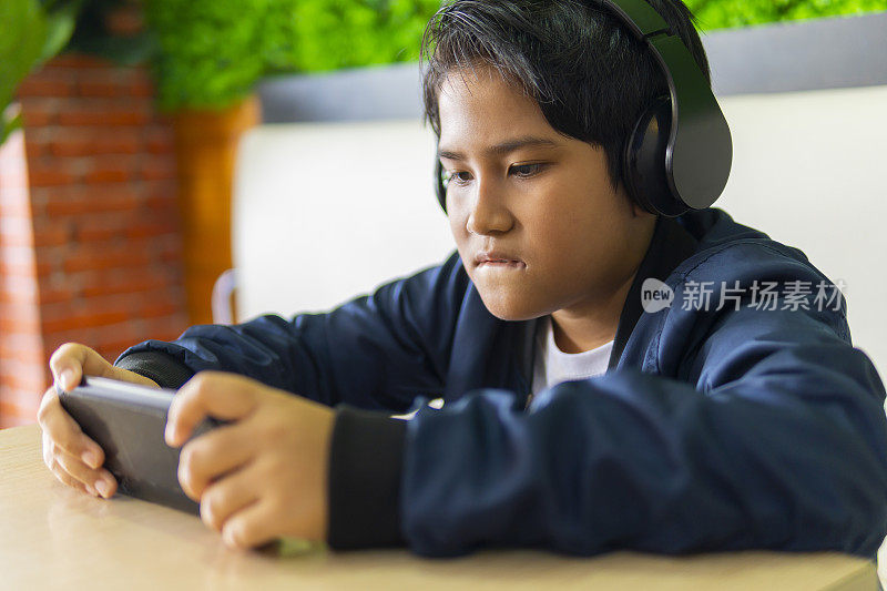 小男孩戴着耳机用智能手机玩游戏