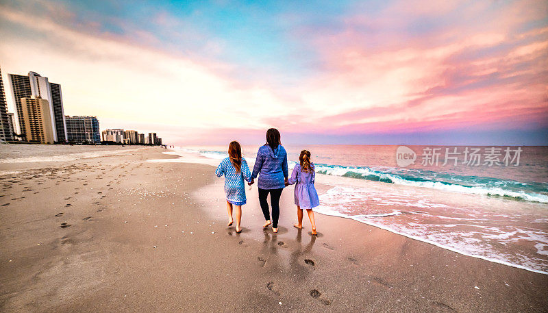 夕阳西下，母亲和两个孩子走在沙滩上