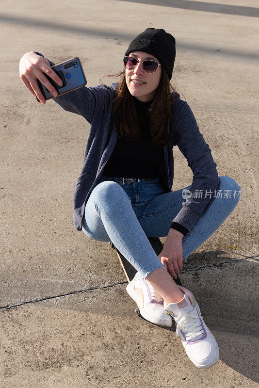 一个休闲的年轻女孩坐在滑板上自拍。