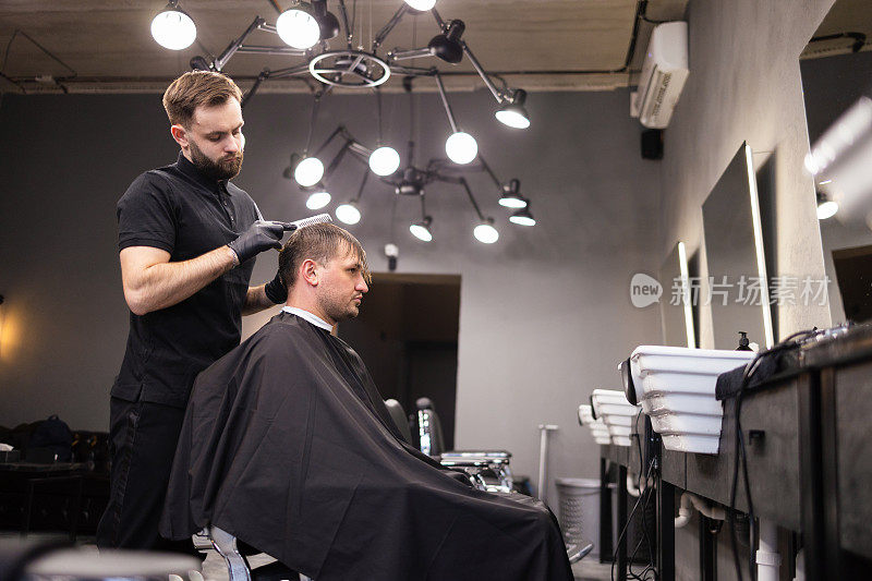 理发师在理发店用发胶和梳子给头发定型。年轻英俊的白人男子在一个现代发廊理发