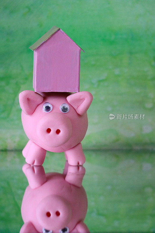 特写图像的小猪银行在镜子表面与粉红色纸板房子背面，五颜六色的海滩小屋，重点是前景，斑驳的绿色背景，家庭财务，房地产和假日储蓄的概念