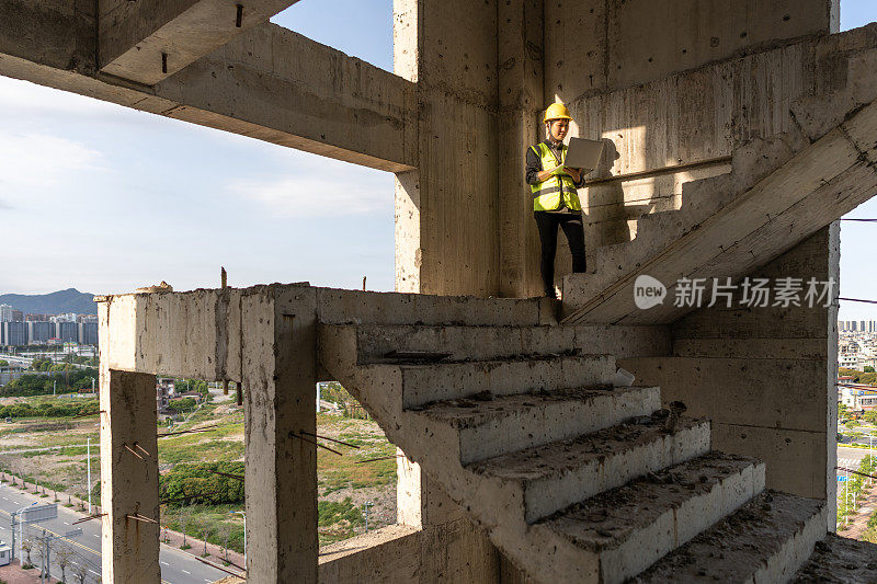 一名亚洲女性建筑工人在工地的楼梯上用平板电脑工作