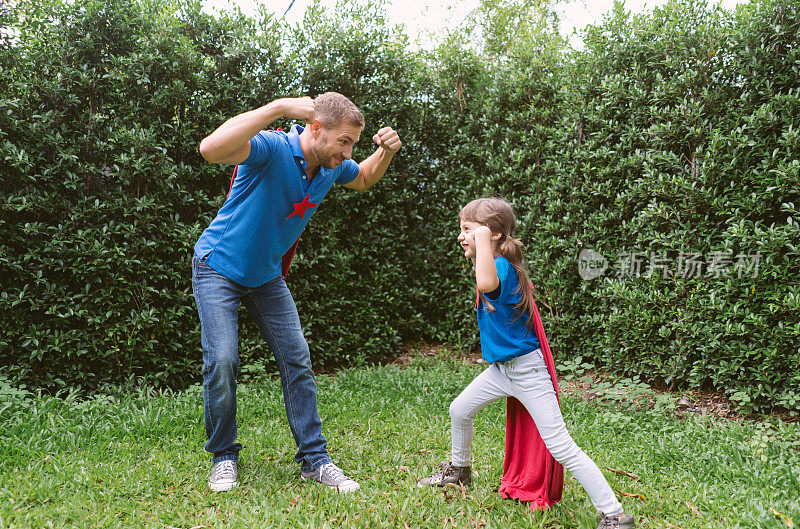 幸福可爱的家庭在一起玩耍。爸爸和穿着超级英雄服装的可爱小女孩在家里的花园里开心地笑着玩耍。家庭假期和在一起享受自由时间。