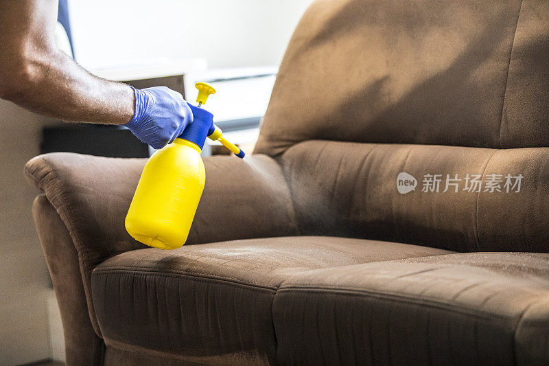 男子在使用湿式吸尘器清洁沙发前喷洒清洁产品