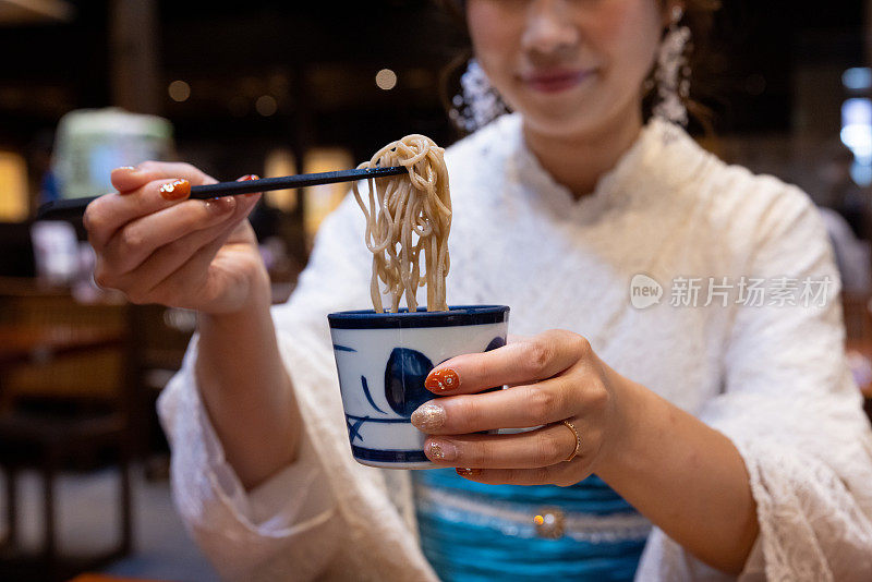 特写和服妇女的手吃荞麦为午餐在日本餐厅