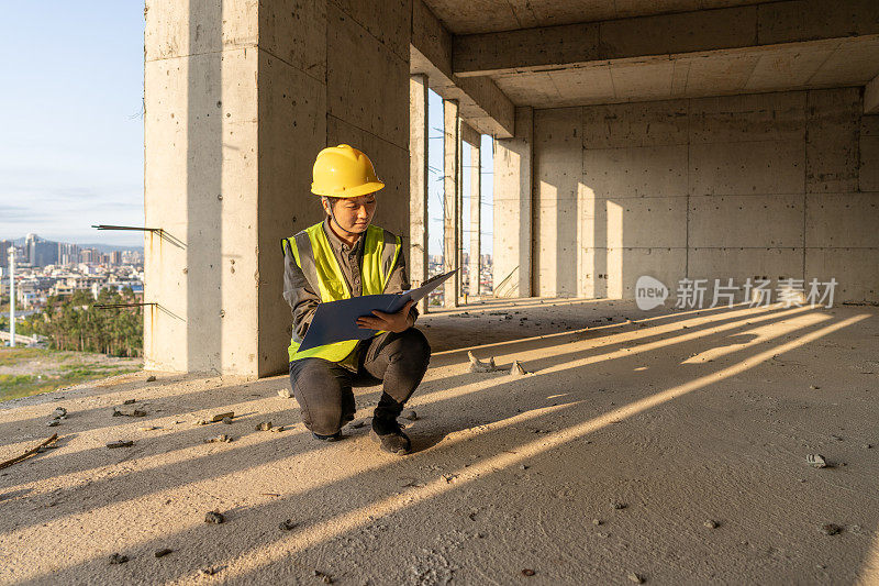 一位亚裔女工程师蹲在建筑工地的地板上看图纸