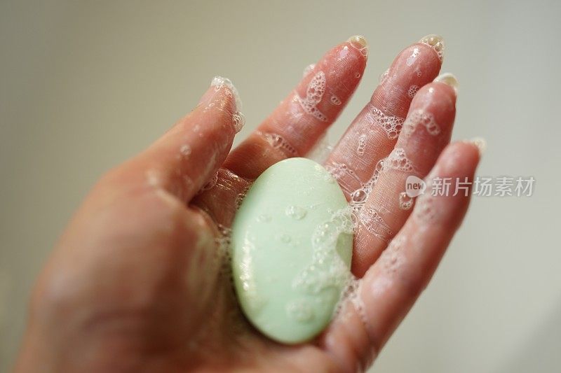在米色背景的湿女性手上有绿色的肥皂条
