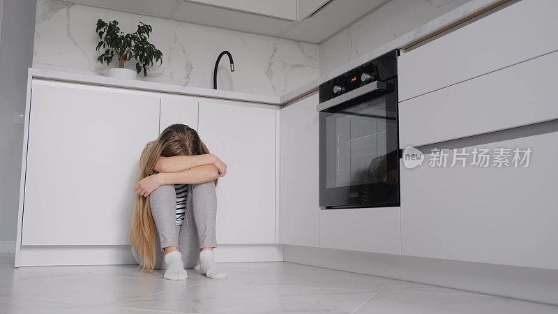 一个患有抑郁症的女人坐在厨房里，她把头埋在膝盖之间。