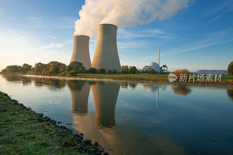 两个冒着热气的冷却塔和核反应堆矗立在清晨的阳光下