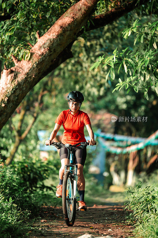 年轻的女子骑着她的山地车在夏日的森林小径上享受美丽的骑行