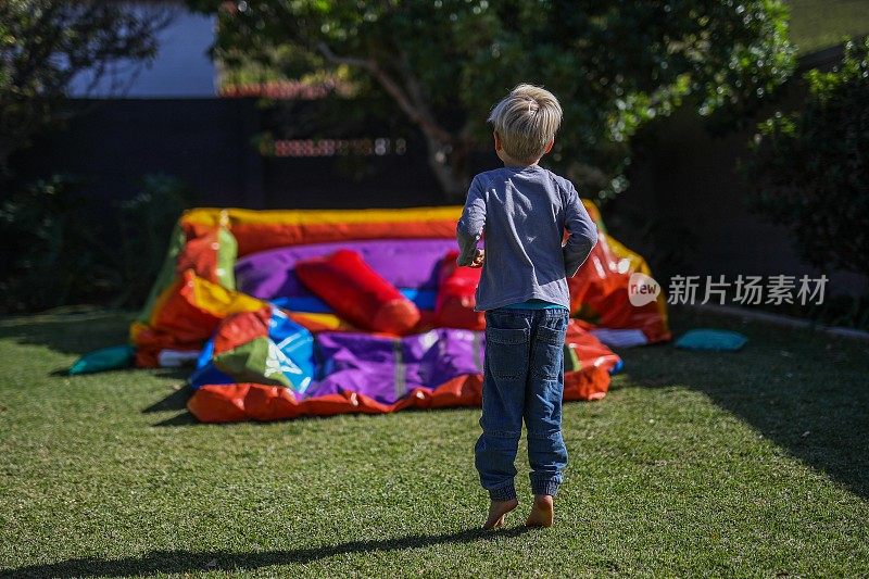 一个小男孩在跳城堡上玩他的生日礼物。