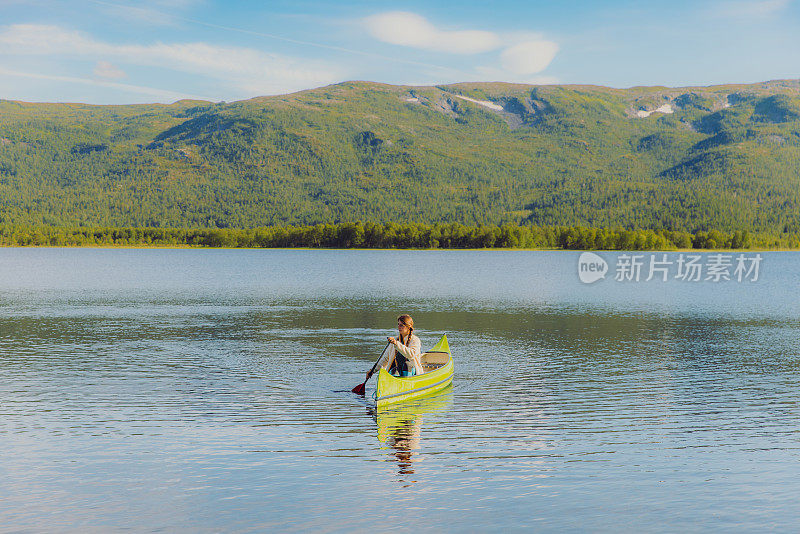 一名女子在挪威风景优美的湖中驾着绿色的独木舟航行