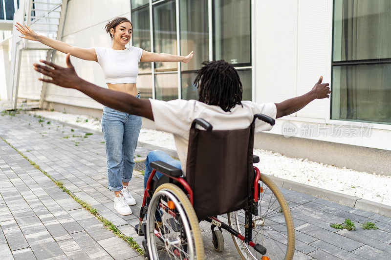 在城市街道上，一名年轻女子跑去拥抱一名坐轮椅的黑人男子