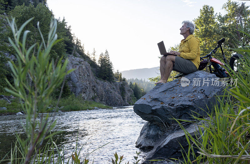一个人在溪流上方的岩石上使用笔记本电脑