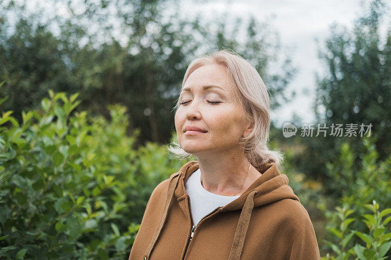 一个放松的白人妇女在绿色的森林里呼吸新鲜空气，闭上眼睛，享受大自然。