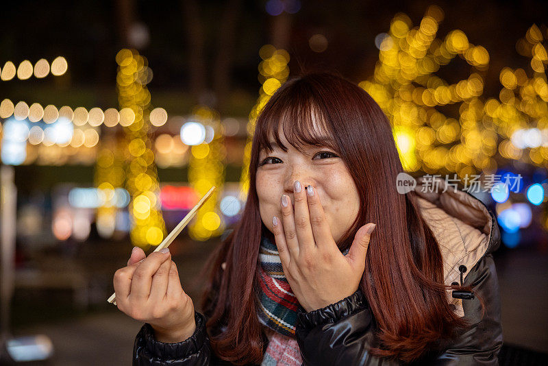 年轻女子在圣诞彩灯下吃东西