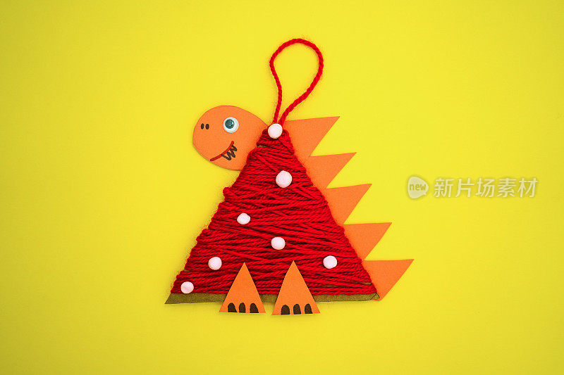 一个孩子用硬纸板和红线做的圣诞树玩具龙躺在黄色的背景上。2024年的象征。教育和手工艺活动。