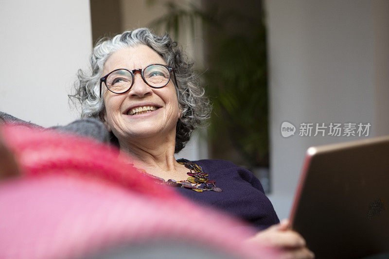 坐在沙发上使用数码平板电脑的微笑女人