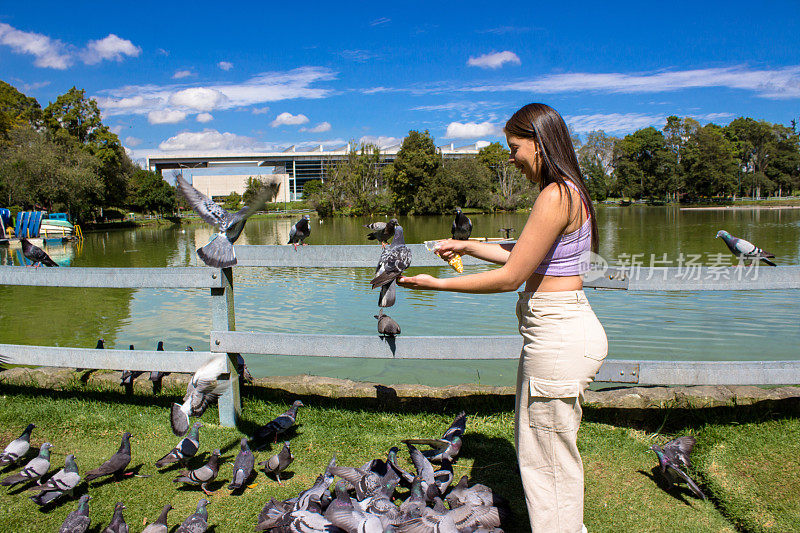 美丽的年轻女子在公园喂鸽子