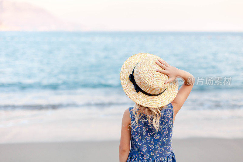 小女孩在海边放暑假。戴草帽的可爱小孩是户外度假胜地的游客。儿童假期，旅游，温柔，女性化的概念。孩子在看海景