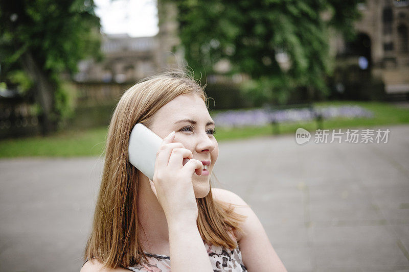 一名年轻女子坐在公园的长凳上玩手机。