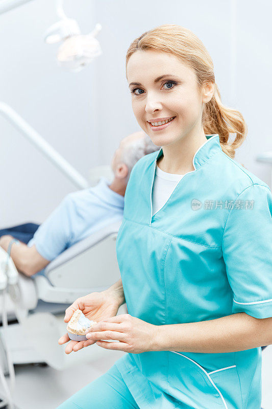 美丽的牙医穿着医疗制服坐在诊所里，对着镜头微笑
