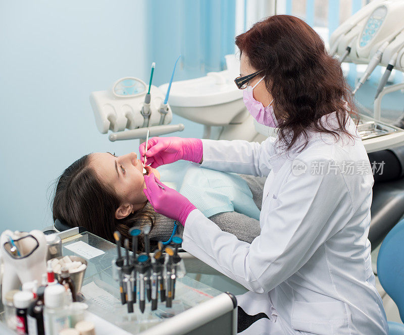 女牙医带着牙科工具-镜子和探针在牙科诊所检查病人的牙齿。医学、牙科和保健概念。牙科设备