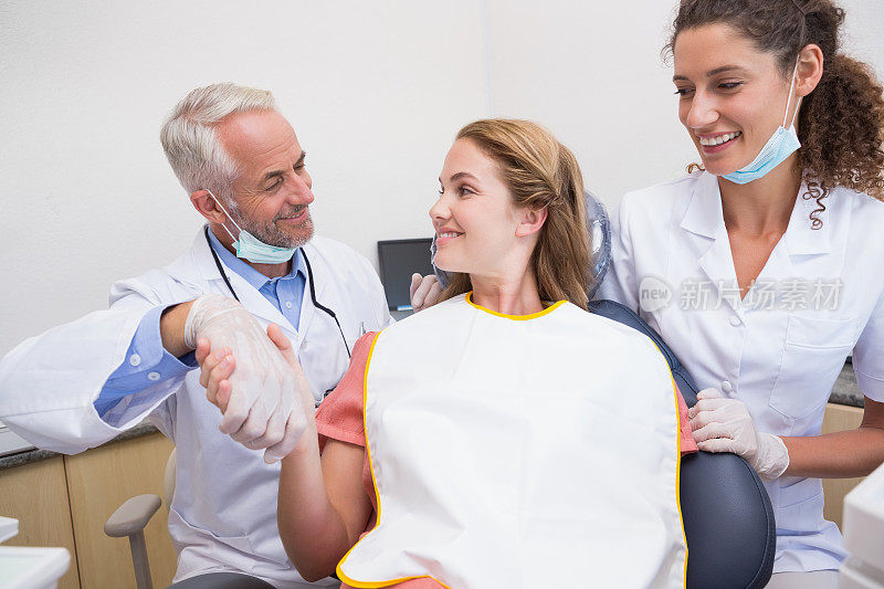 牙医在助手旁边的椅子上和病人握手