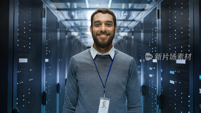 一个古玩，积极和微笑的IT工程师站在一个大数据中心服务器室中间的肖像。